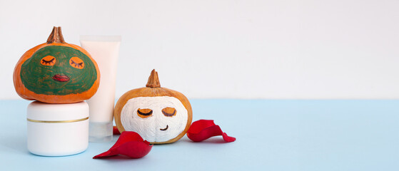 Naklejka premium Pumpkins with drawn faces, spa supplies, rose petals and clay masks on blue table