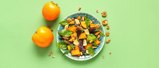 Plate of delicious salad with persimmon, pomegranate seeds and walnut on green background