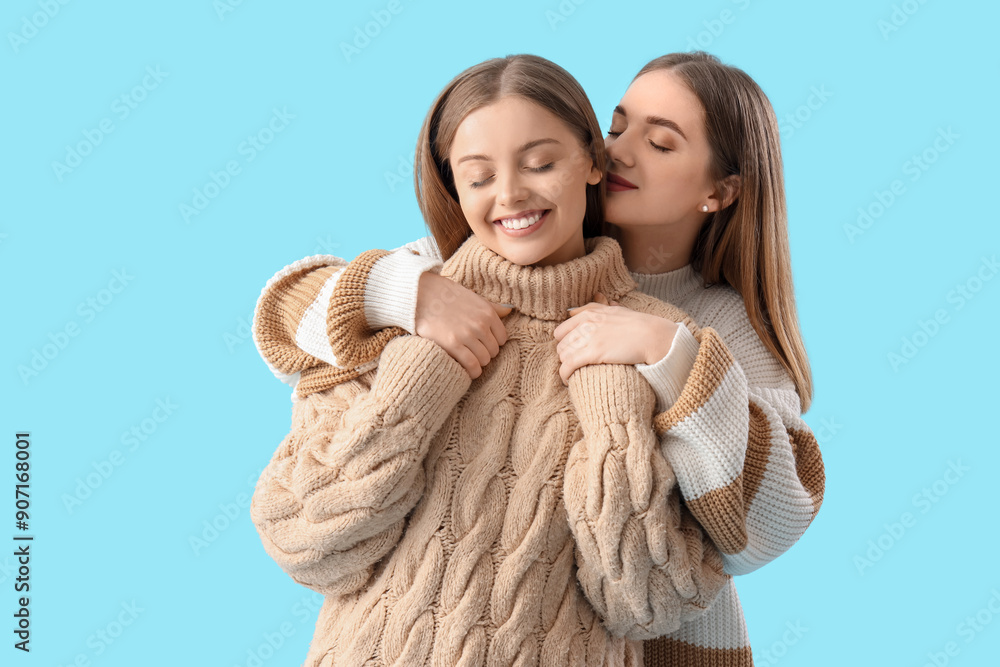 Sticker Young lesbian couple in warm sweaters hugging on blue background