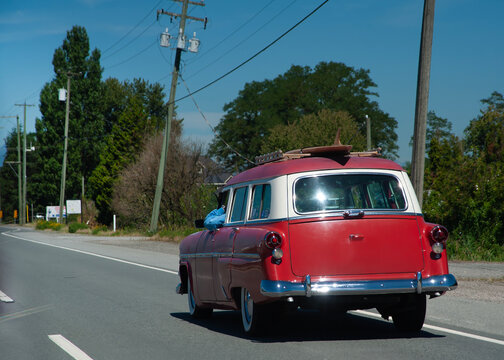 Vintage station wagon with surfboard traveling on a road.