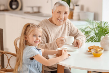 Cute little girl with her granny drinking tea at table in kitchen