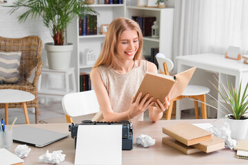 Female author with book and vintage typewriter at table in office