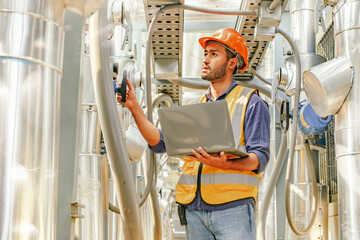 Male HAVC refrigeration system technician stands holding laptop recording preventative inspection refrigeration equipment refrigerant level control valve into the system and checking leaks at various.