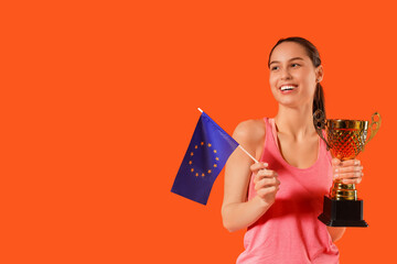 Sporty young woman with gold cup and flag of European Union on orange background