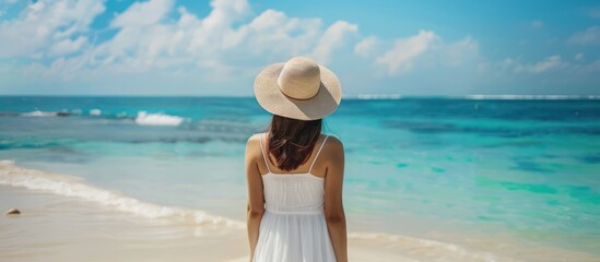 Woman in white dress and sun hat standing on tropical beach, enjoying ocean view. Concepts. travel, vacation, summer, relaxation, paradise
