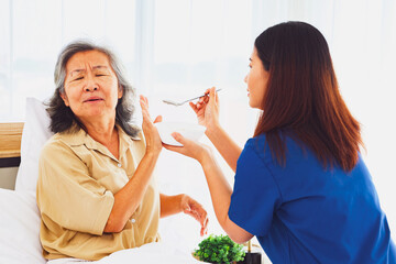 Sick elderly woman uses her hands refuse eat porridge that female nurse tries feed her breakfast...
