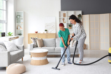 Little African-American boy with his mother cleaning carpet at home