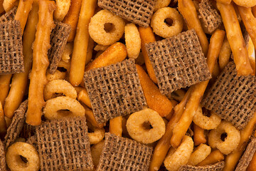Close-up view of a variety of snack items, including pretzel sticks, ring-shaped cereal, and square-shaped cereal with a grid pattern.