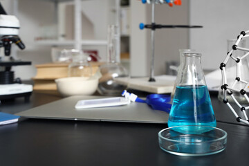 Petri dish and chemical flask with blue liquid on table in medical laboratory, closeup