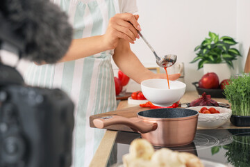 Young woman pouring soup into bowl while recording cooking video class in kitchen, closeup