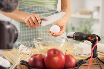 Female blogger breaking egg while recording cooking video class in kitchen, closeup
