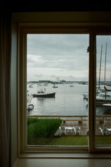 Fototapeta premium Scenic view of boats docked in a marina through a window on a cloudy day
