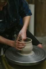 Person shapes pottery on a spinning wheel in a workshop, focusing on the hands and clay.