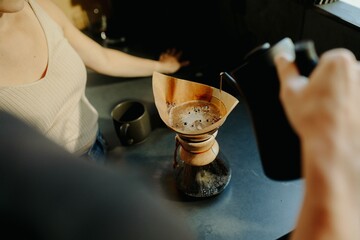 Person making pour-over coffee while another person watches