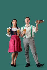 Young happy couple in traditional German clothes with glasses of beer and snacks on green background