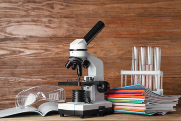 Modern microscope with chemical flasks, copybooks and protective glasses on table against wooden background