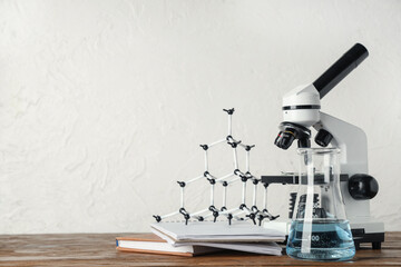 Modern microscope with chemical flask, molecular model and notebooks on wooden table against white...