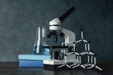 Modern microscope with chemical flask, books and molecular model on wooden table against grey...