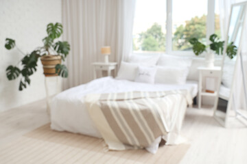 Blurred view of light bedroom with cozy bed and monstera leaves