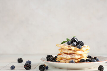 Delicious Belgian waffles with blueberries, blackberries and sugar powder on plate on table against white background