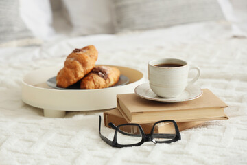 Tasty breakfast with books and eyeglasses on bed, closeup
