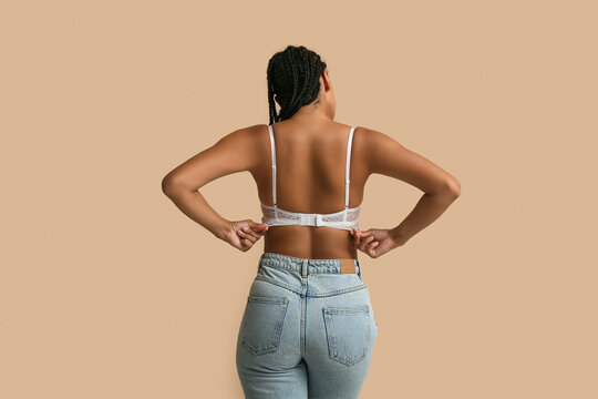 Young woman in bra on beige background, back view