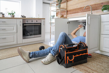 Male plumber fixing sink in kitchen