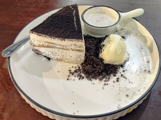A slice of delicious, layered crepe cake with a generous topping of chocolate crumbs, served with a scoop of vanilla ice cream and a small pitcher of cream.