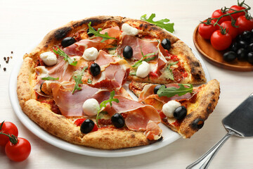Tasty pizza with cured ham, olives, mozzarella cheese, tomatoes and arugula on light wooden table, closeup