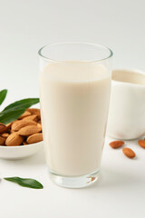 Fresh almond milk in glass, nuts and green leaves on white background