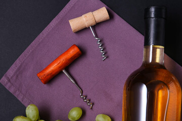 Corkscrews, wine and grapes on black background, flat lay
