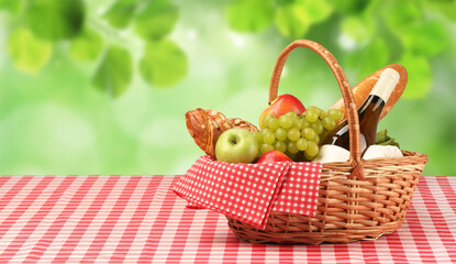 Picnic basket with foods and wine on table in nature. Space for text