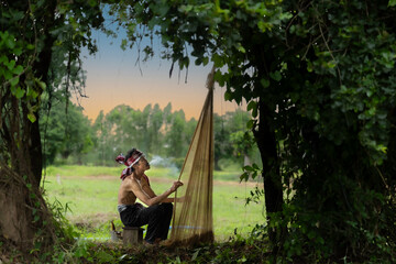 Asian fisherman sitting on wooden chair smoking and checking net before catching freshwater fish in nature river at the countryside.Life style and rural life concept.