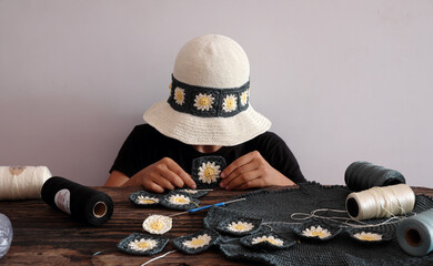 Woman wear daisy motifs crohet hat, surrounded by an array of colorful supplies materials for diy project, leisure with creativity handmade in workspace © xuanhuongho