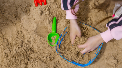 A child girl playing in the sandbox at the playground outdoors. Little girl playing with sand molds and making mud pies. Outdoor creative activities for kids.
