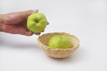 Someones hand is picking up green guavas in a fruit basket on a white background