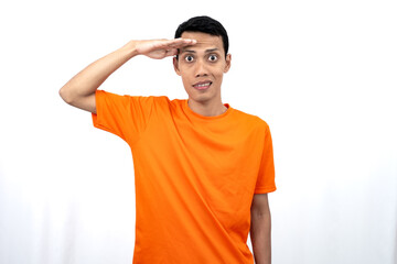 Portrait of a young Asian man wearing an orange t-shirt looking surprised, shocked and shocked. Hands are near eyes, isolated on white background.