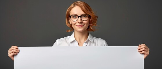 Smiling woman with glasses holding a blank white signboard against a dark background, ideal for business and educational presentations.