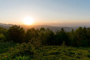 Sunset over forested hills with sky.