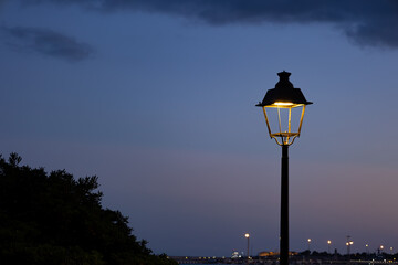 Landscape of a city at dusk with streetlights in the distance and one in the center of the image,...