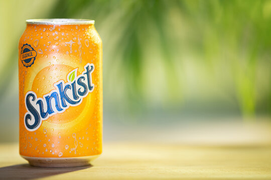 Vibrant and refreshing can of Sunkist orange which is covered in condensation droplets on a wooden table  with a blurred, green background, suggesting a natural, outdoor setting.