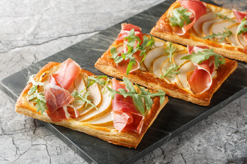 Snack open puff sandwiches with pear, jamon and arugula close-up on a marble board on the table. Horizontal