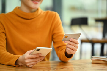 Cropped shot of smiling young Asian woman holding mobile phone and credit card for financial transaction