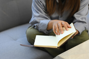 Relaxed young woman sitting on grey couch and reading book, spending leisure tine at home