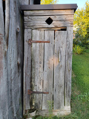 The rustic wooden outhouse wychodek with a weathered door, situated in a rural area