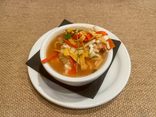 A small bowl of chicken tortilla soup topped with cheese, tortilla strips and cilantro.