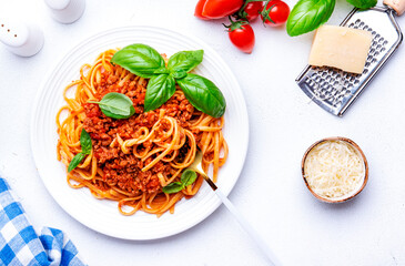 Prepared spaghetti in bolognese sauce or pasta with minced meat and tomatoes decorated green basil, white table background, top view