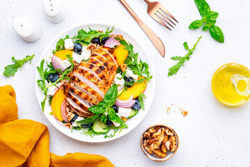 Gourmet summer fresh salad with peaches, chicken, blueberries, onion, feta cheese, basil and arugula, white background, top view