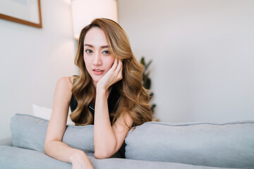 Naklejka premium beautiful modeling woman touching cheek act. relax beautiful gorgeous woman sitting on couch gesturing. beautiful female model posing looking gently cheek pose on comfortable sofa with eye contact