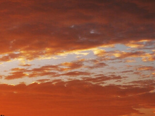 a breathtaking sunset with a dramatic sky filled with thick, textured clouds. The clouds, predominantly dark and foreboding, are illuminated by a vibrant orange and red glow, creating a stark contrast